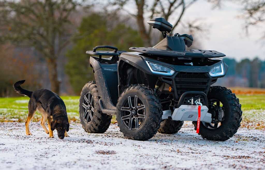 Segway Snarler AT6 Black Edition står parkerad utomhus på frostbeklädd mark med en schäferhund i förgrunden. Den svarta designen med grova däck och frontvinsch framhäver modellens kraft och exklusiva utrustningsnivå.